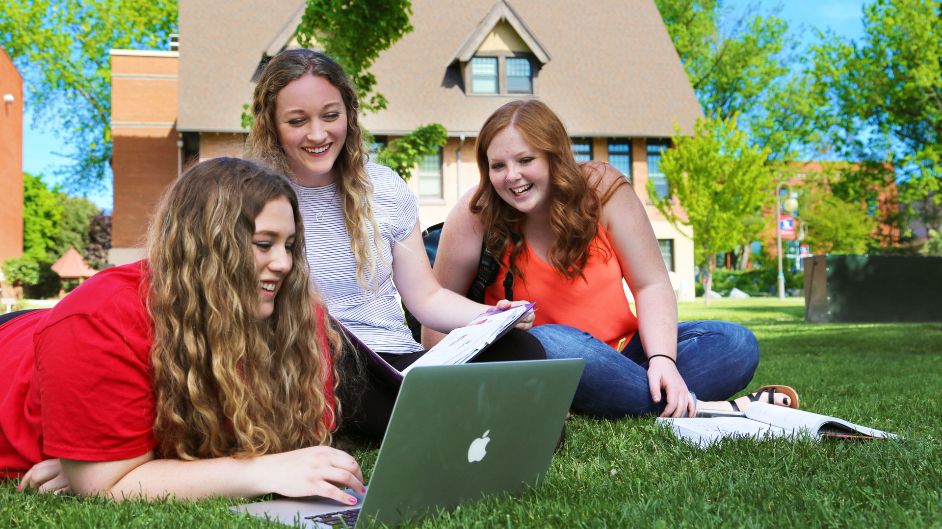 Three female students sitting on grass looking at laptop